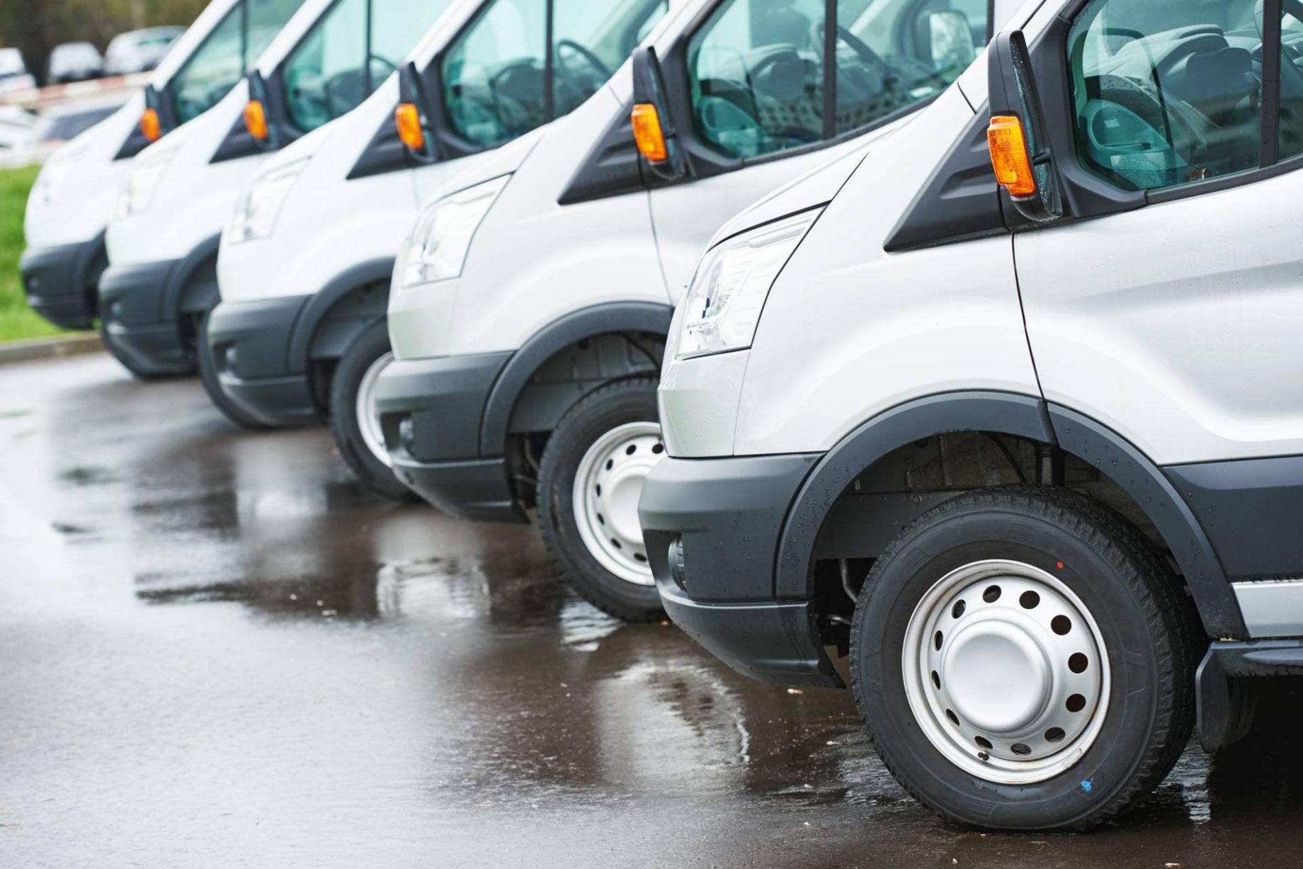 A row of white vans parked on a wet pavement