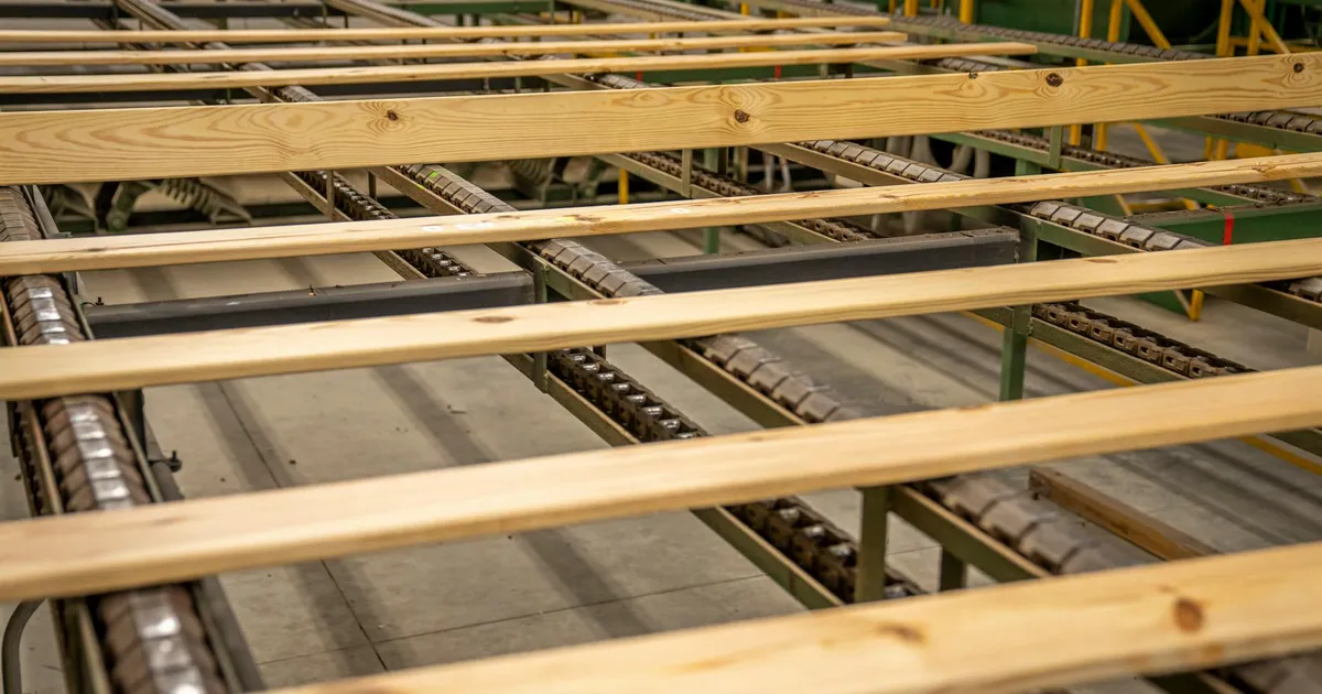 Close-up of wooden planks on a production conveyor in a factory setting.