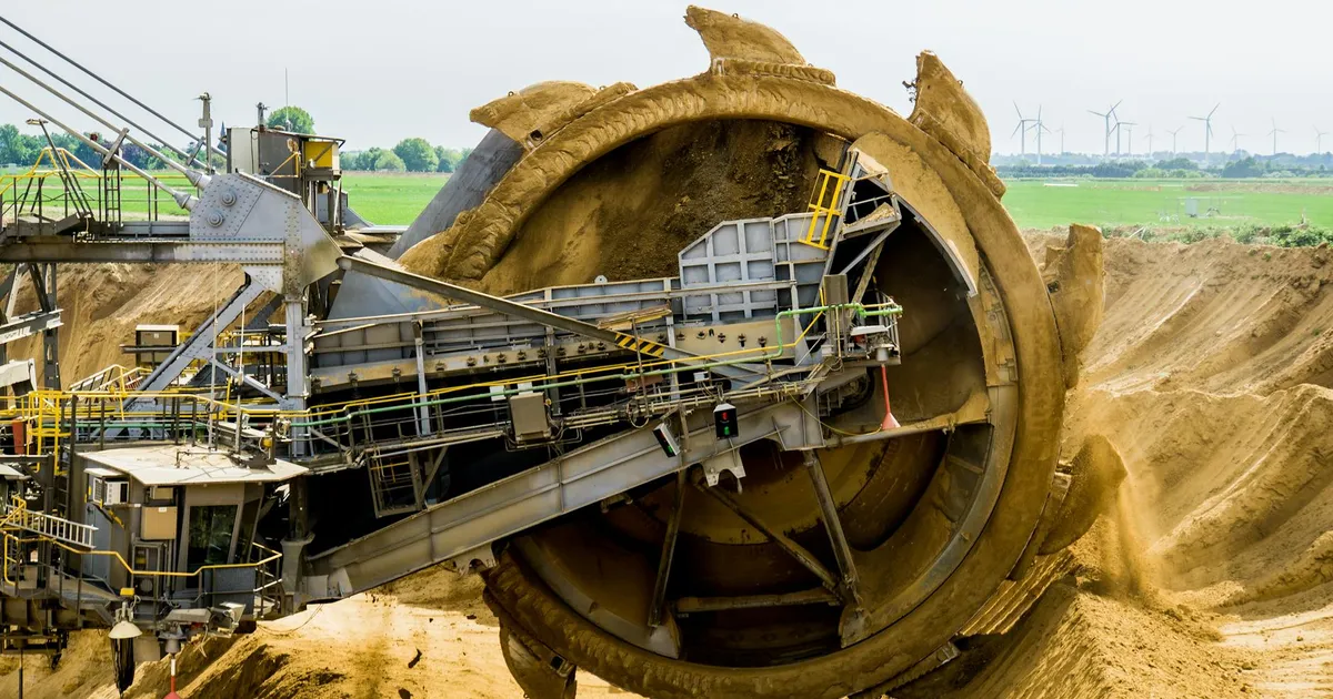 A large bucket wheel excavator working in an open pit mine against a green landscape.