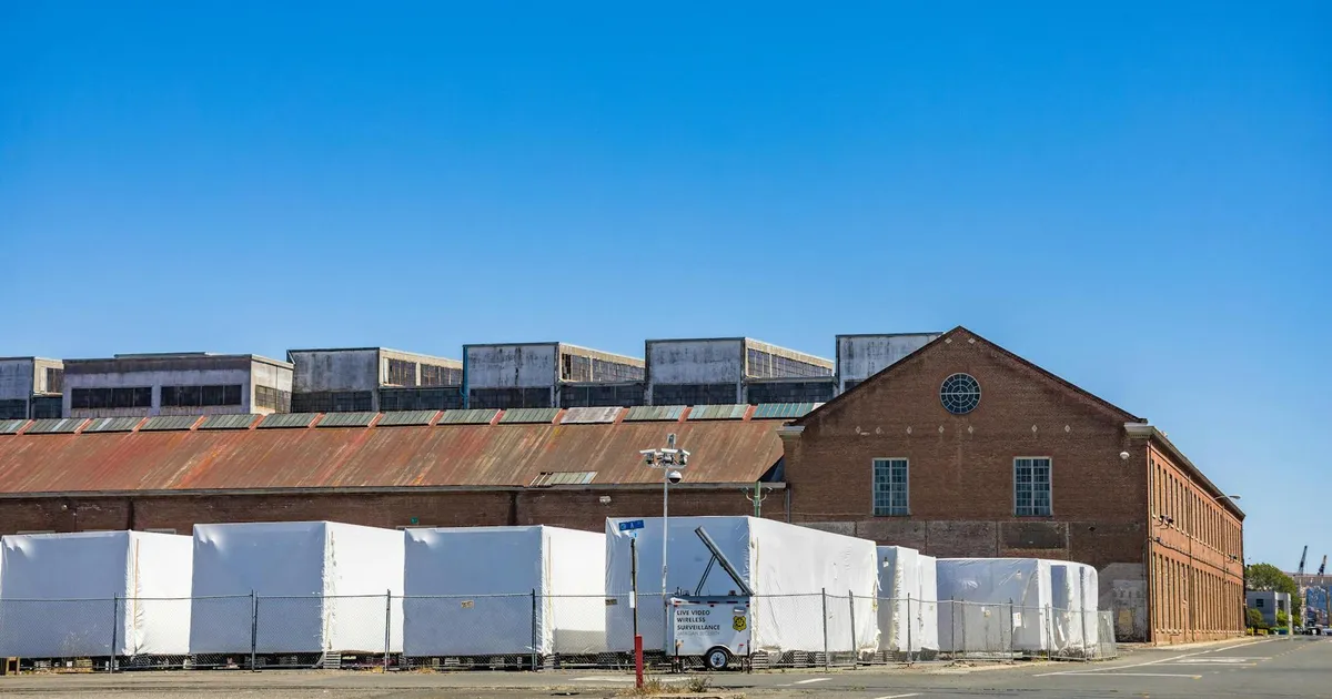 A brick warehouse with white covered storage against a clear blue sky on an empty street.