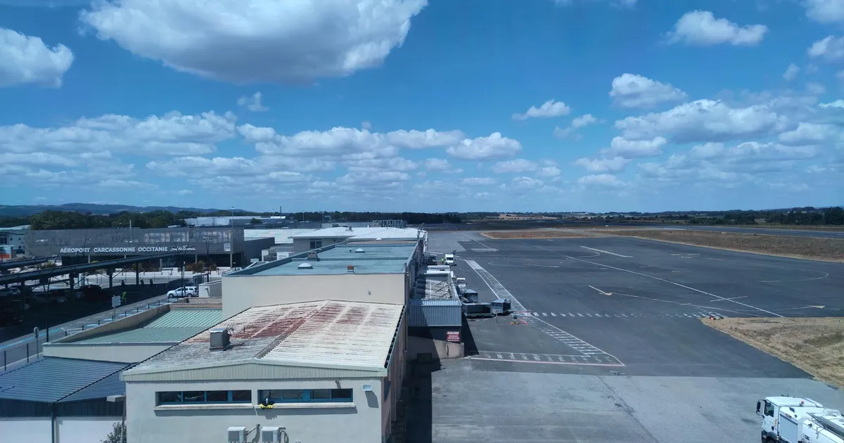 Aerial view of a sunny airport with runway and terminal buildings under blue sky.