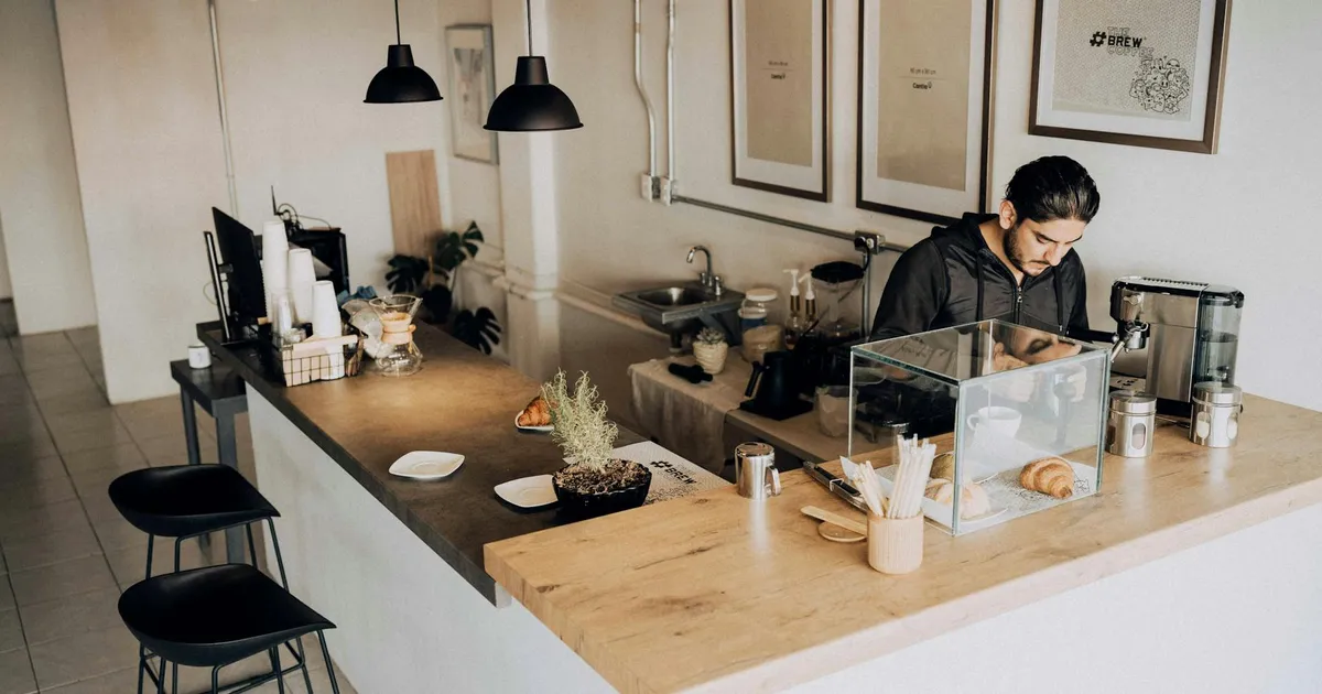 A barista works in a modern café with minimalistic décor and warm lighting.
