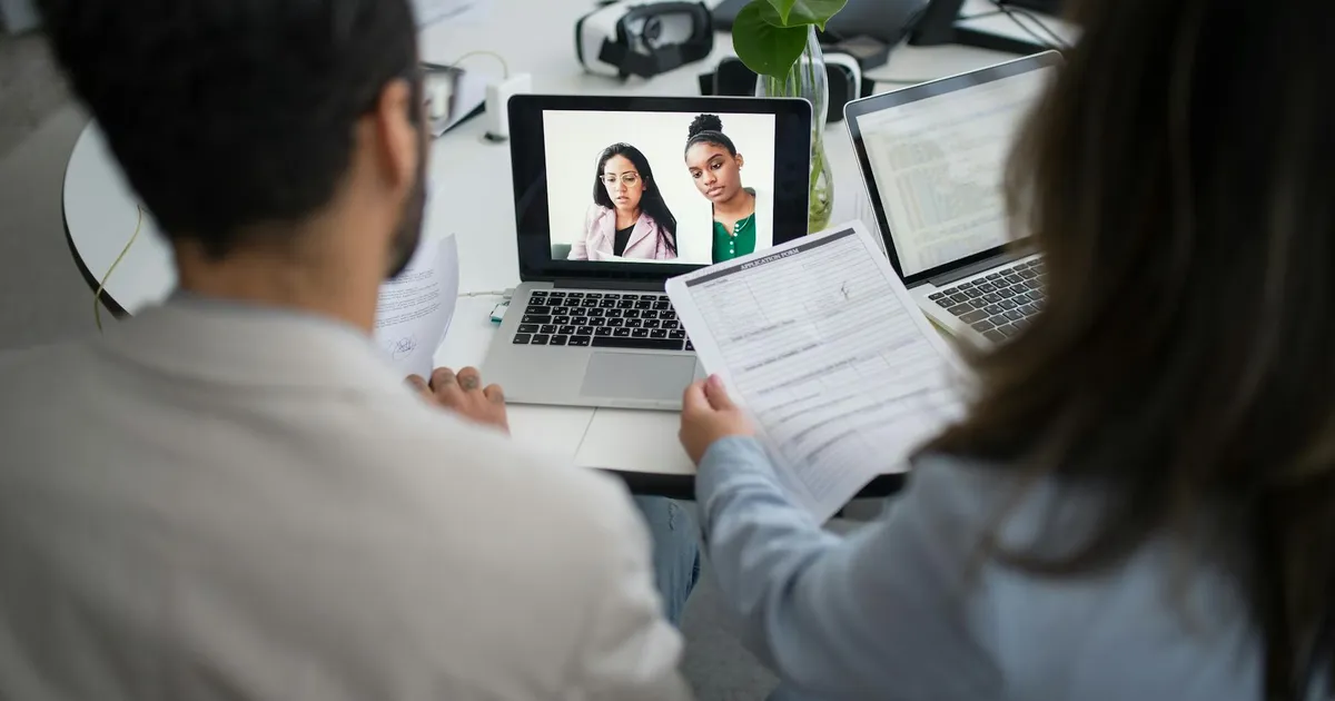 Two professionals conduct a virtual job interview using laptops in a modern office.