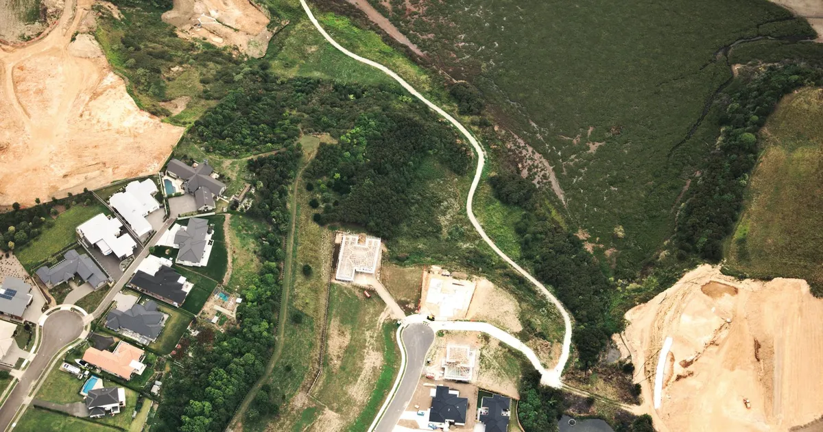Aerial shot of a suburban housing development with roads, green spaces, and construction sites.
