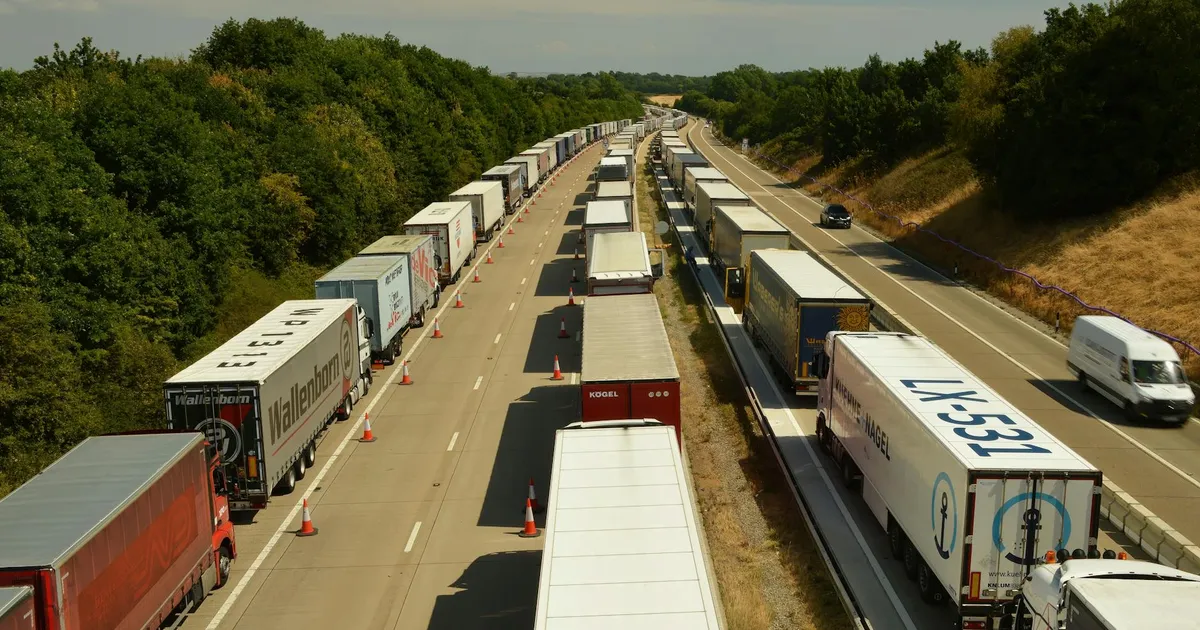 A high-angle shot of trucks and trailers in traffic on a highway in England beneath a bright sky.