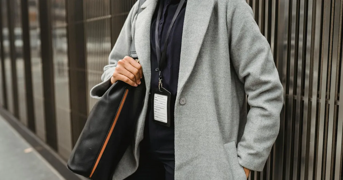 Crop anonymous female employee with badge standing with hand in pocket and shoulder bag on city pavement