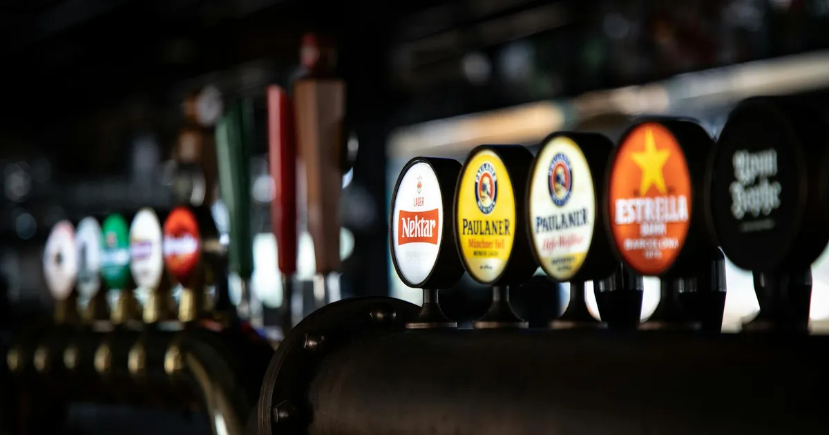 Close-up of assorted beer taps in a dimly lit bar, showcasing various brewery logos and selections.