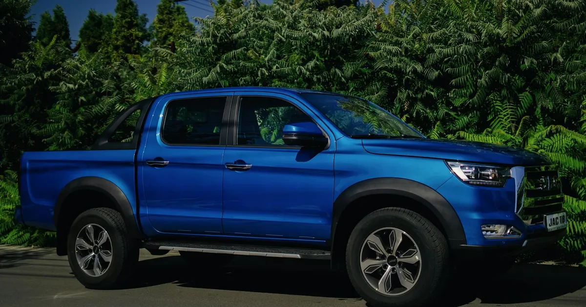 A blue pickup truck parked on a sunny day in Kyiv, Ukraine, surrounded by lush greenery.