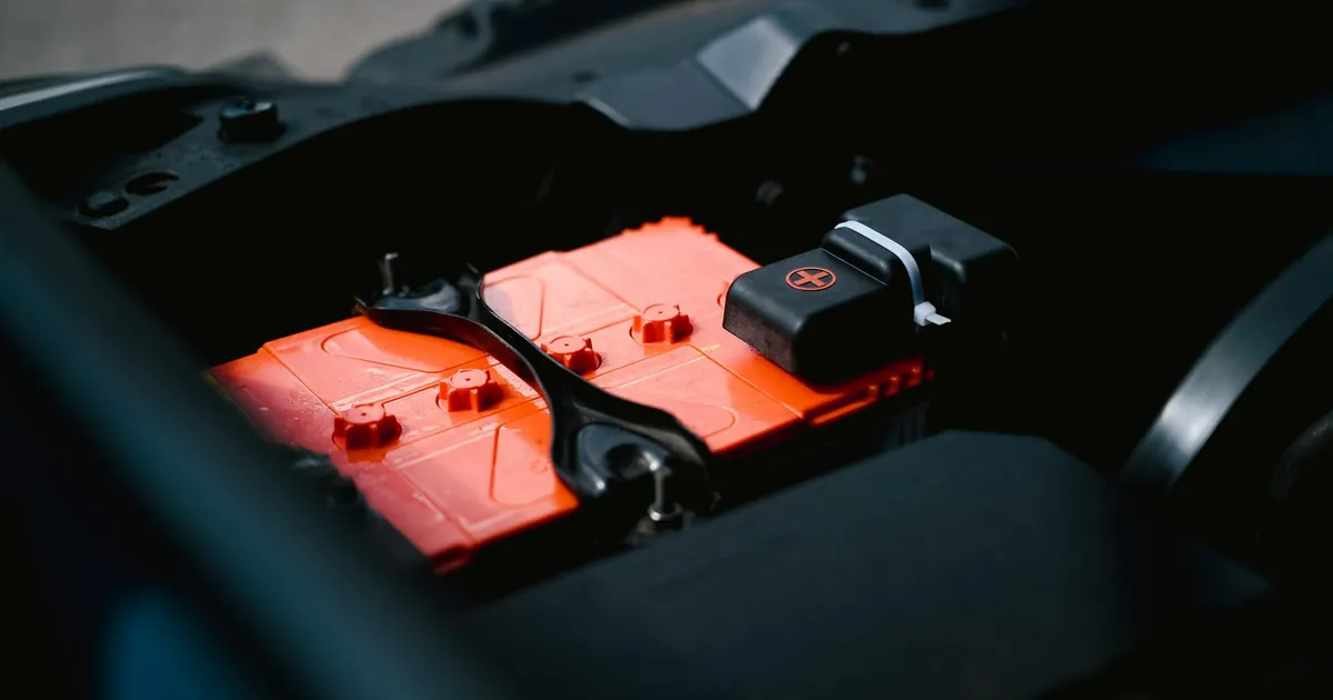 Detailed view of an orange car battery inside a vehicle's engine bay, highlighting its features.