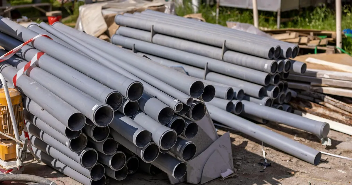 A collection of gray PVC pipes neatly stacked at an outdoor construction site.