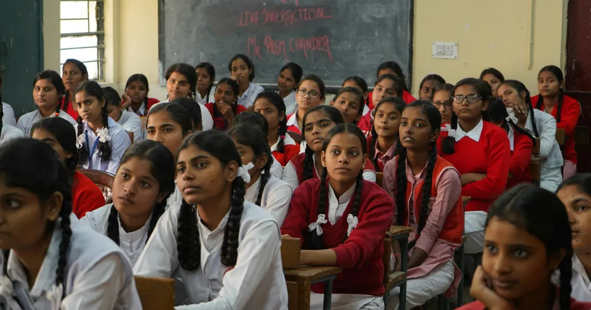 Group of Indian schoolgirls in uniform attentively listening in a classroom setting.