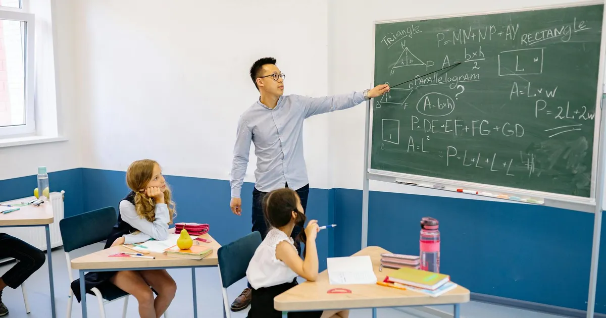 Teacher pointing at chalkboard with students in classroom learning geometry.