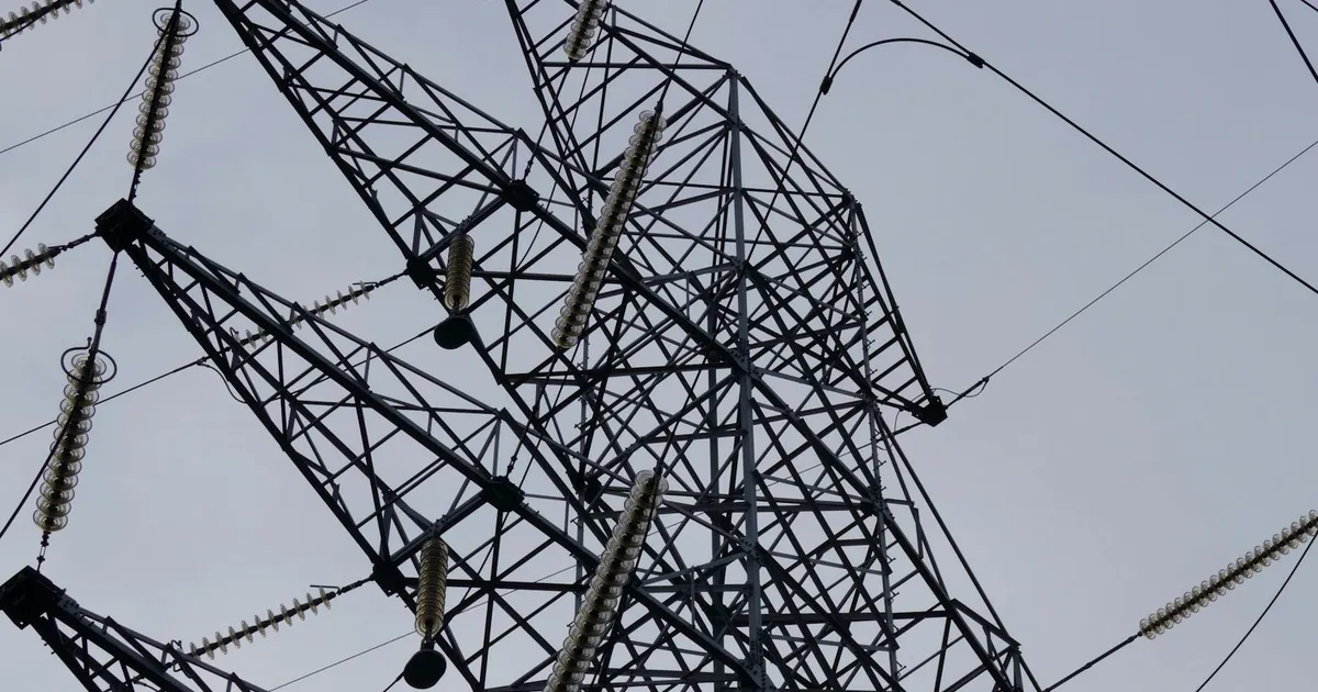 Low angle shot of a metal power transmission tower with cables against a clear sky.
