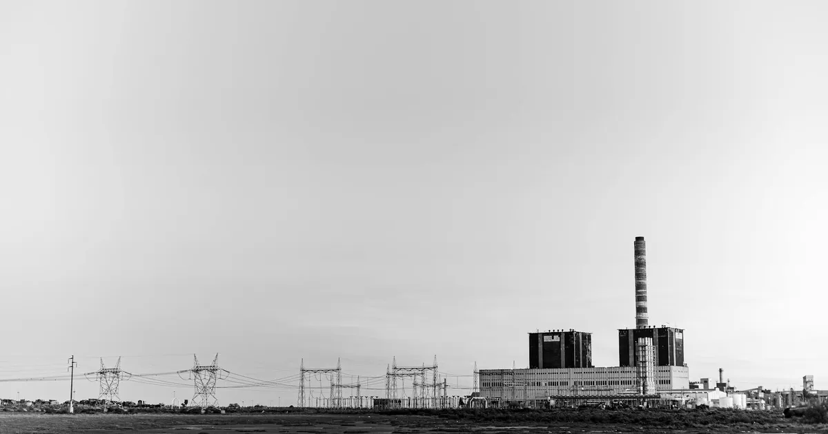 Black and white photo of a power plant with transmission lines, capturing urban industrial scenery.