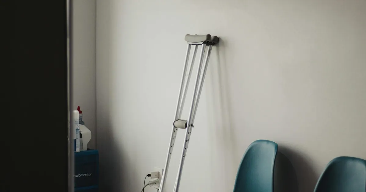 Crutches resting against a wall in a minimalist waiting room with blue chairs.