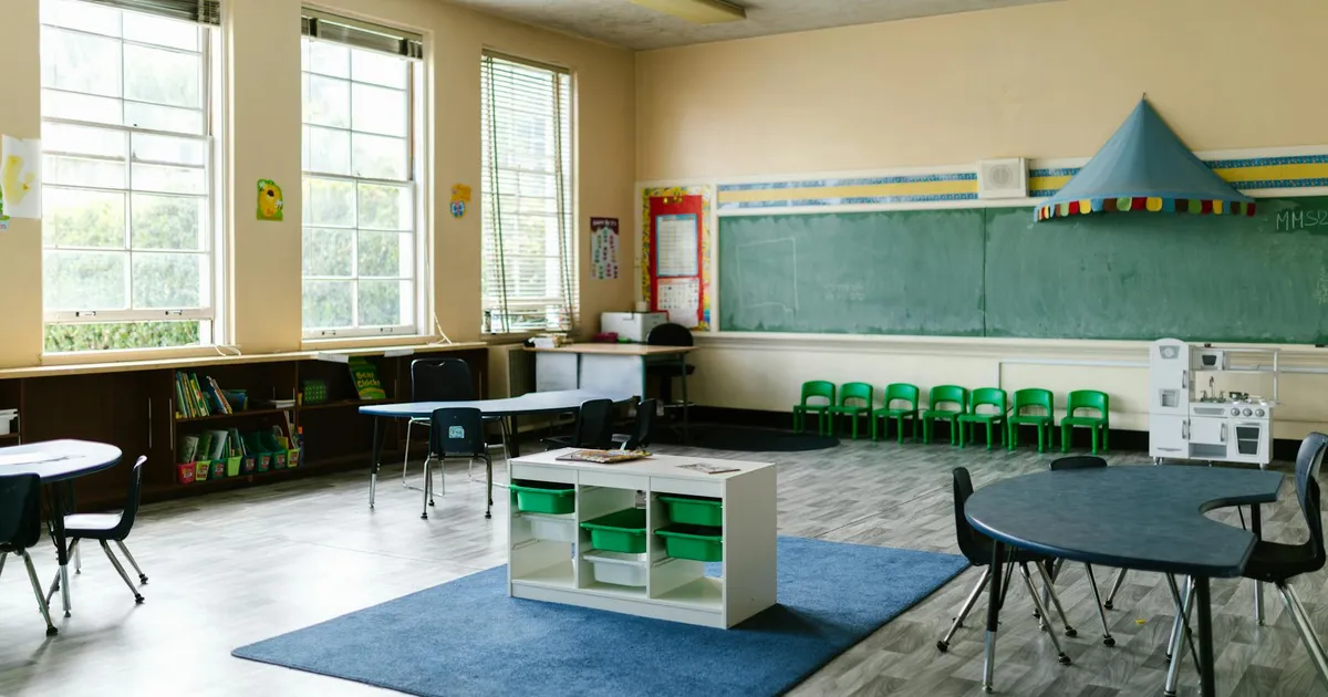Spacious preschool classroom interior with tables, chairs, and a chalkboard for a learning environment.