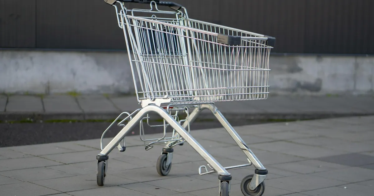 A solitary metal shopping cart stands in an empty outdoor parking lot, capturing the essence of consumerism.