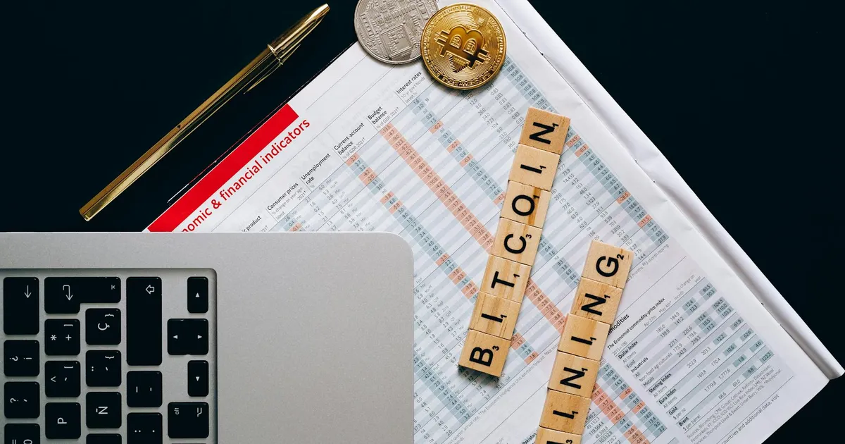 Top view of a laptop, Bitcoin coins, and financial indicators symbolizing Bitcoin mining and investment.