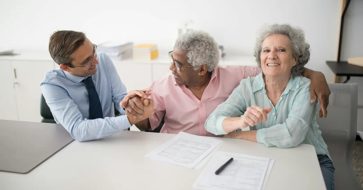Senior couple in office meeting with consultant, discussing financial documents and smiling.