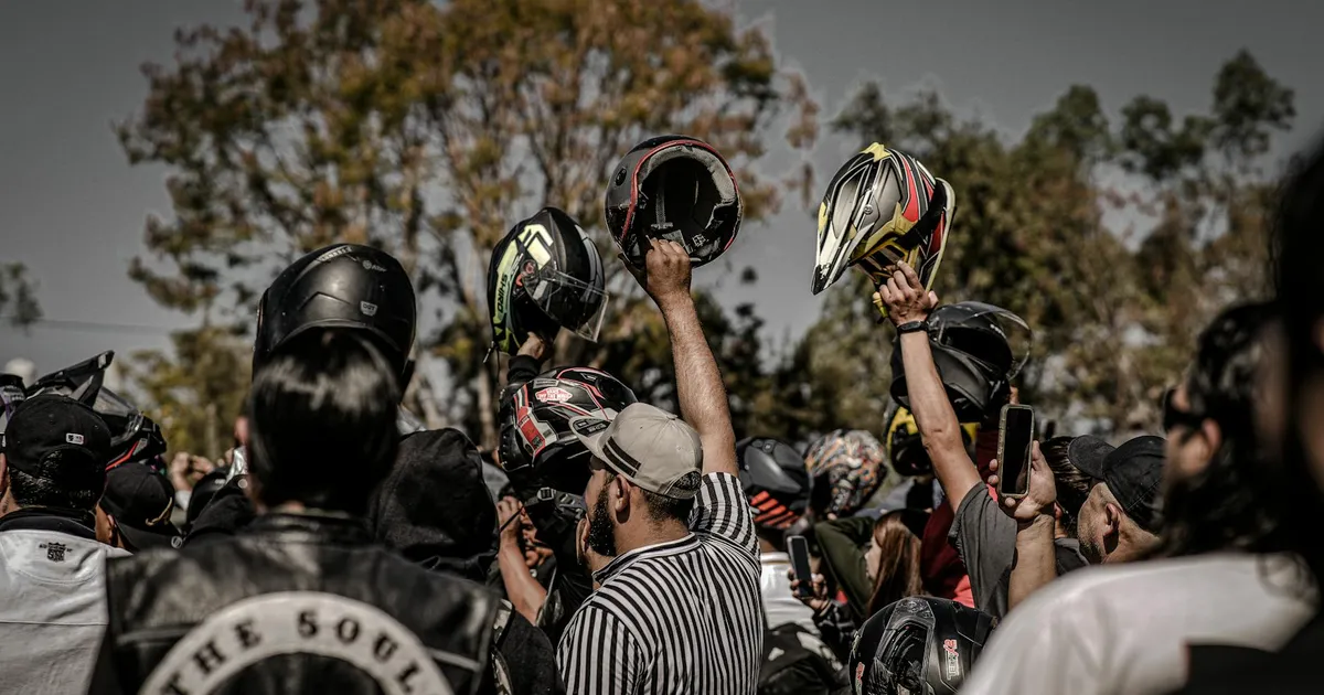 A lively outdoor gathering of motorcyclists raising their helmets in celebration or unity.