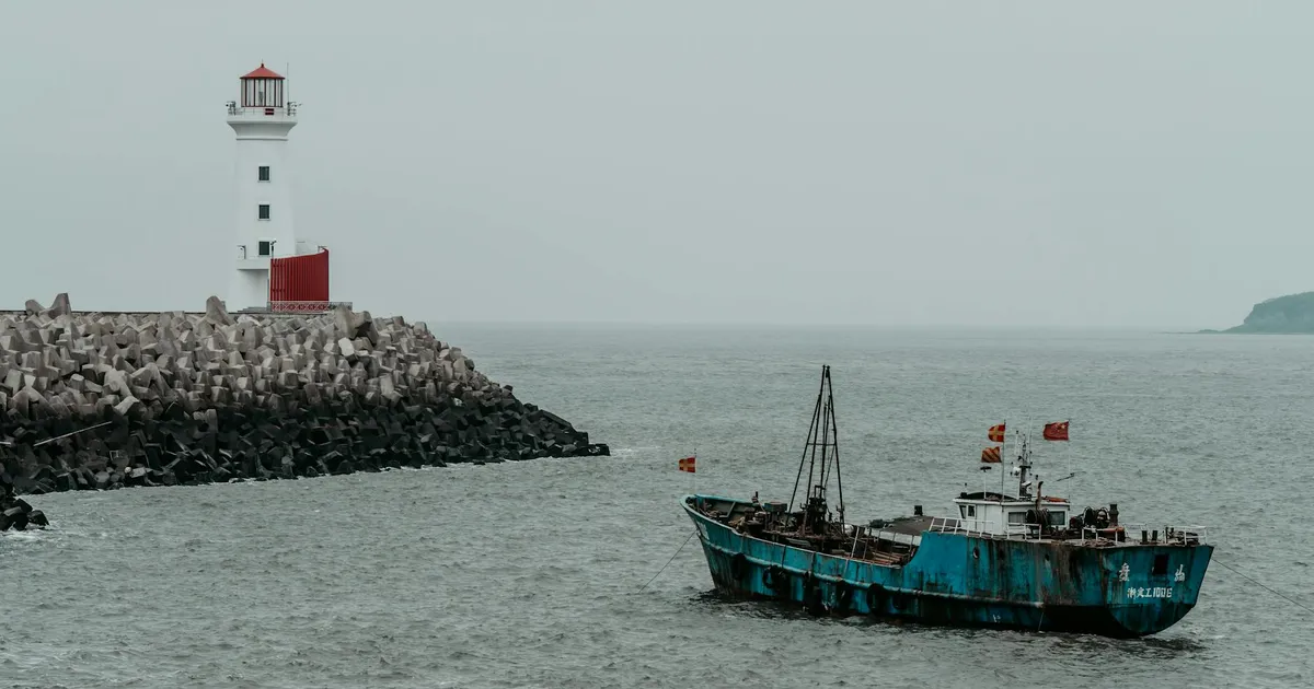 A serene coastal scene with a lighthouse and a fishing vessel in calm waters.
