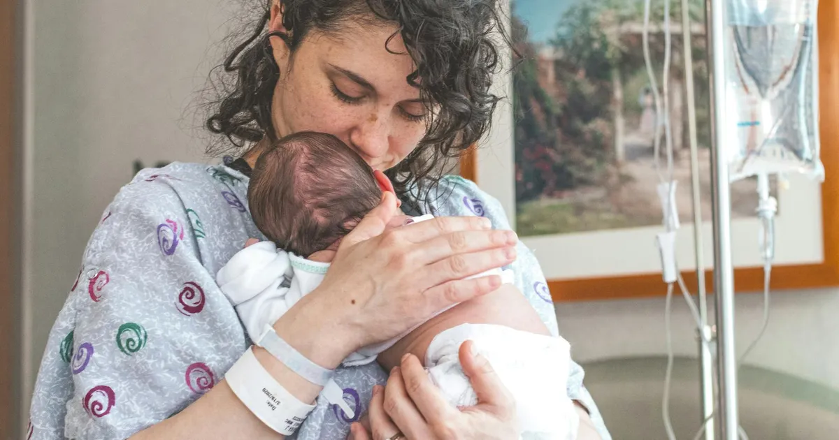 Mother gently holding newborn baby in hospital setting, showcasing warmth and love.
