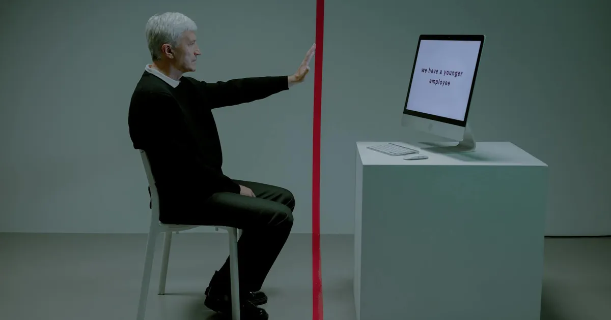 Senior man facing age discrimination in workplace, seated opposite a computer.
