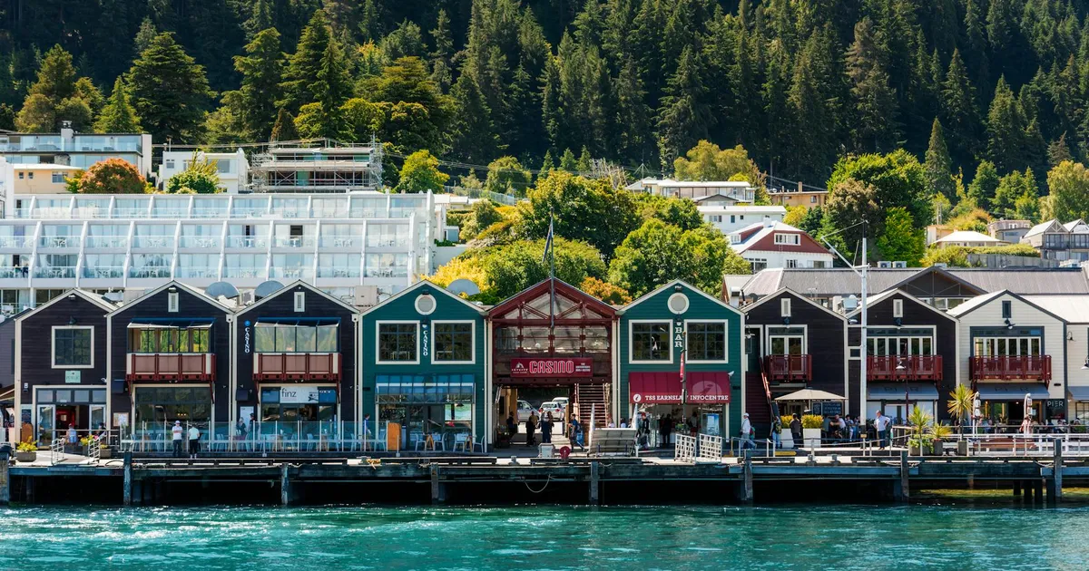Colorful waterfront buildings in Queenstown with mountainous backdrop and vibrant greenery.
