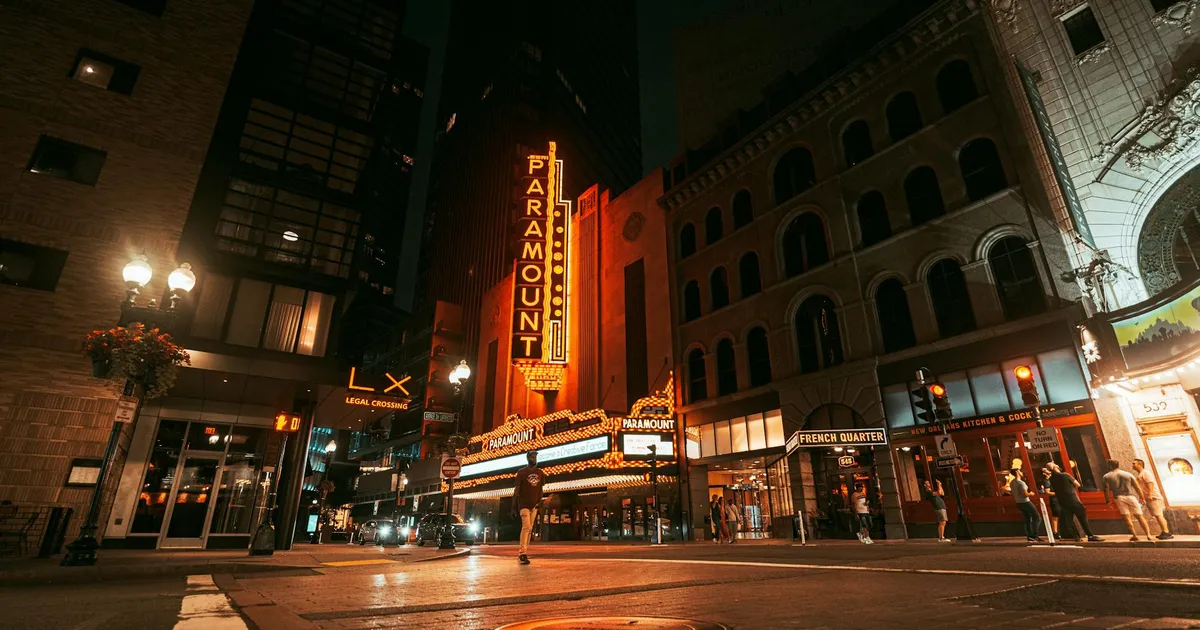 A nighttime street scene featuring the iconic Paramount Theater in Boston, illuminated by bright neon lights.