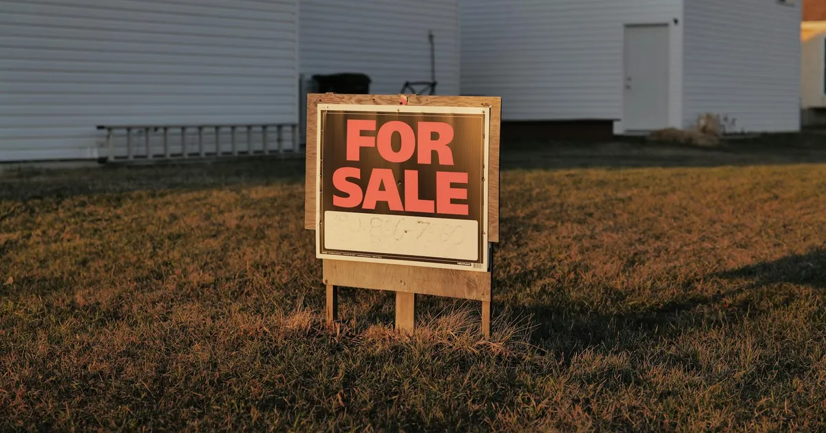 Close-up of a 'For Sale' sign in a suburban yard, indicating a property for sale.