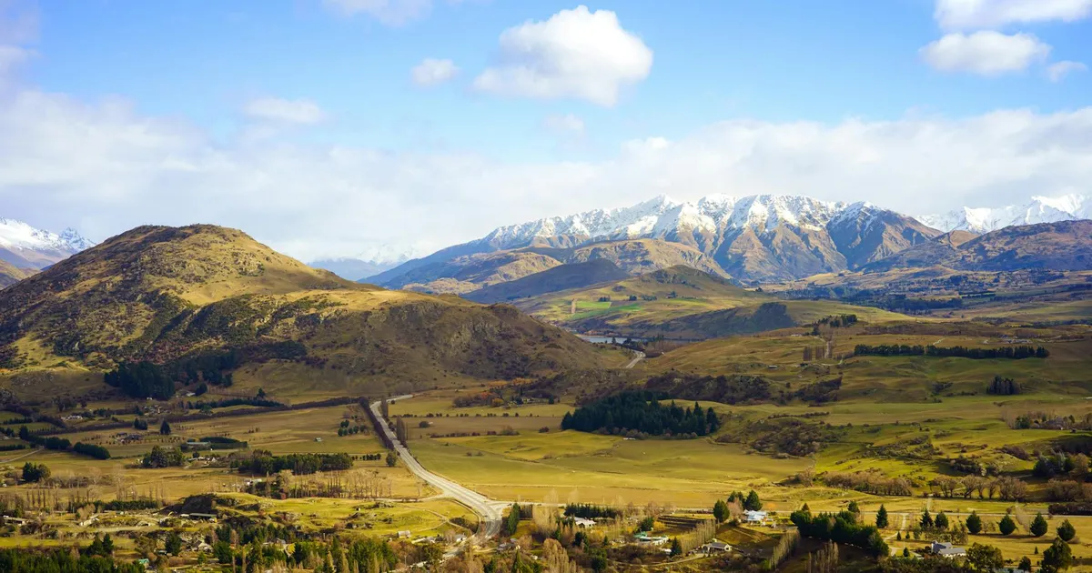 Breathtaking aerial view of Queenstown's rural landscape with hills and snow-capped mountains.