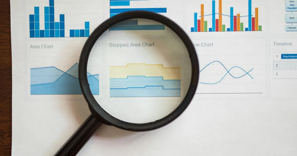 A magnifying glass focuses on various business charts and graphs on paper.