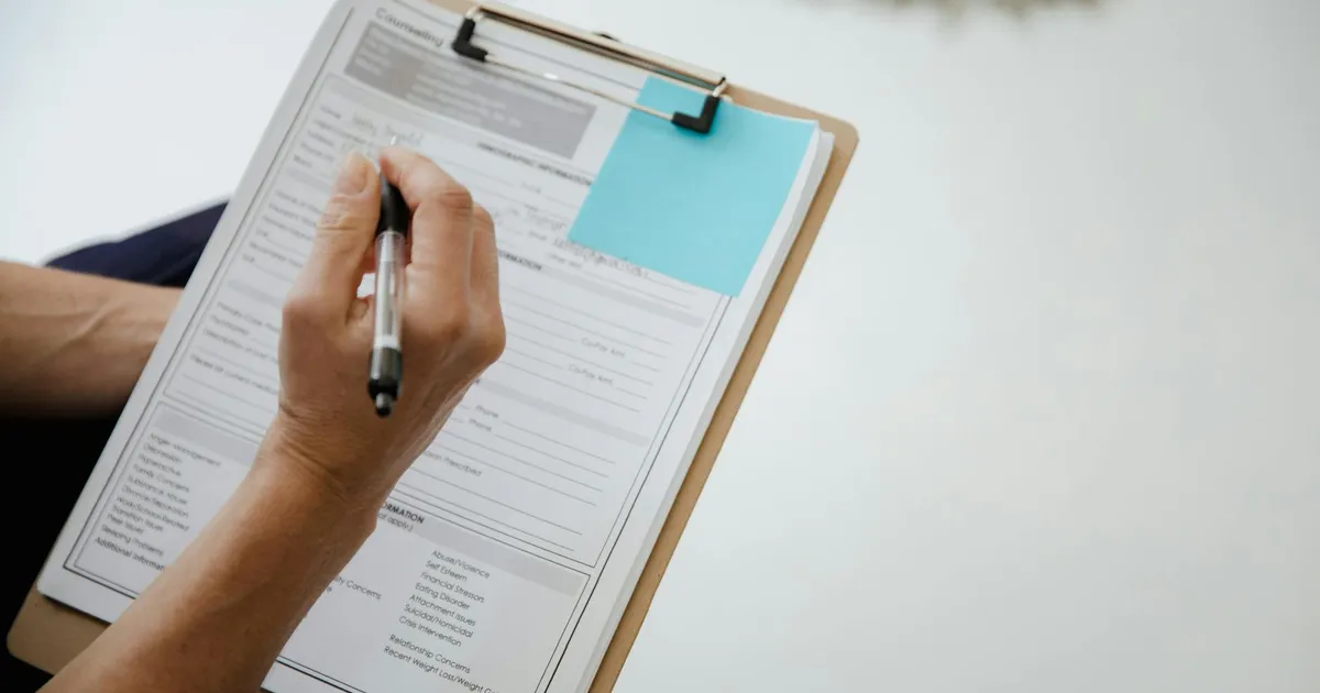 A person writes on a document using a clipboard indoors.
