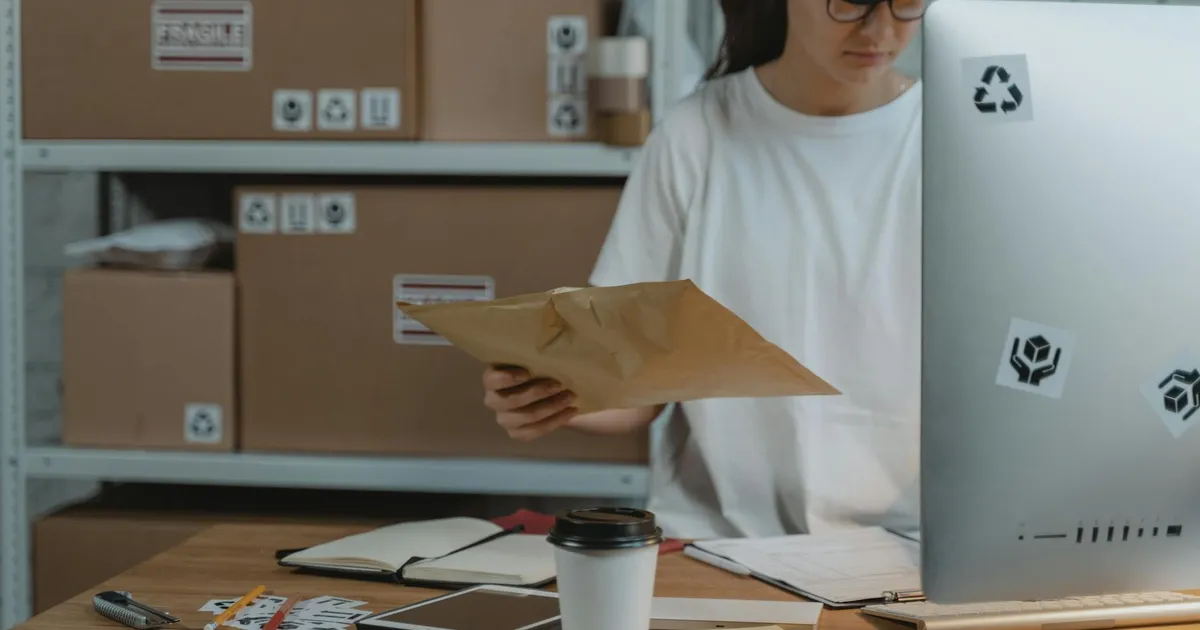 Woman sorting parcels at her desk in a logistics office, demonstrating efficient workspace organization.