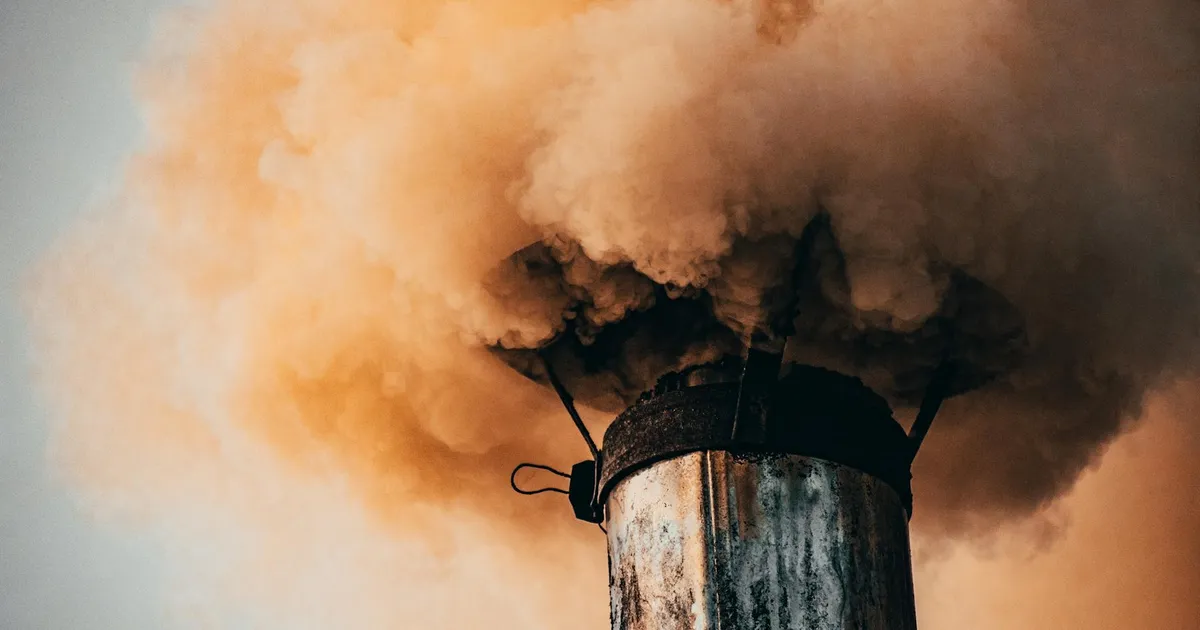 A close-up of a factory smokestack releasing thick smoke into the air, illustrating industrial pollution.