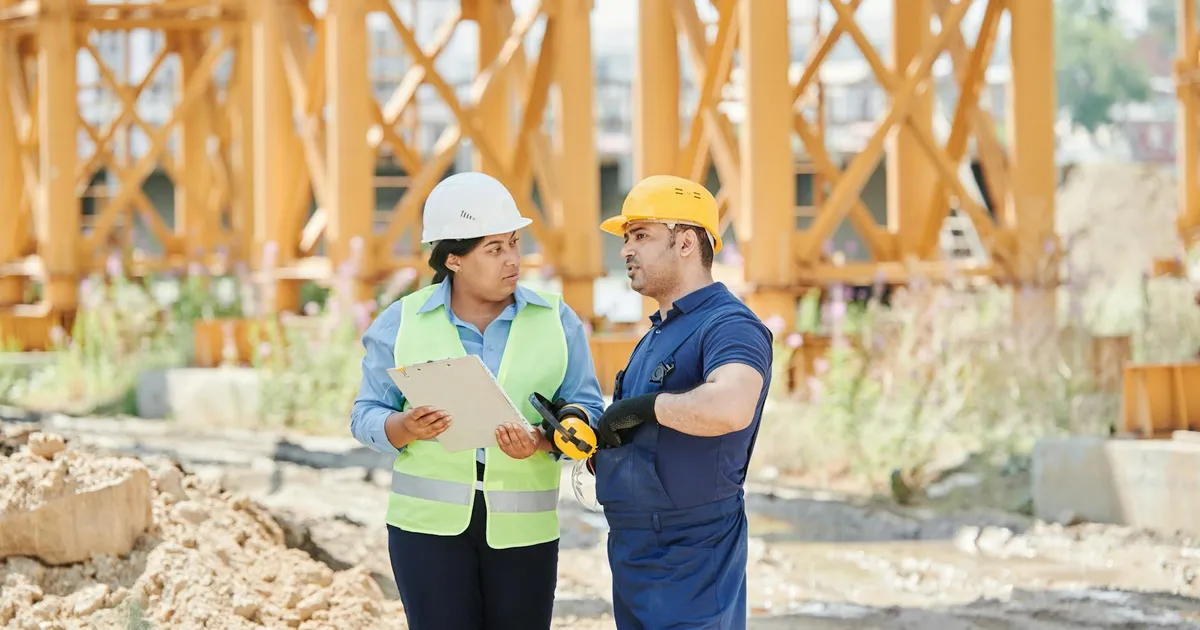 Construction workers engaged in a discussion at a construction site wearing safety gear.
