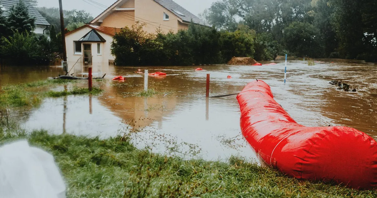 Flooded residential area protected by red flood barriers, showing severe weather impact.