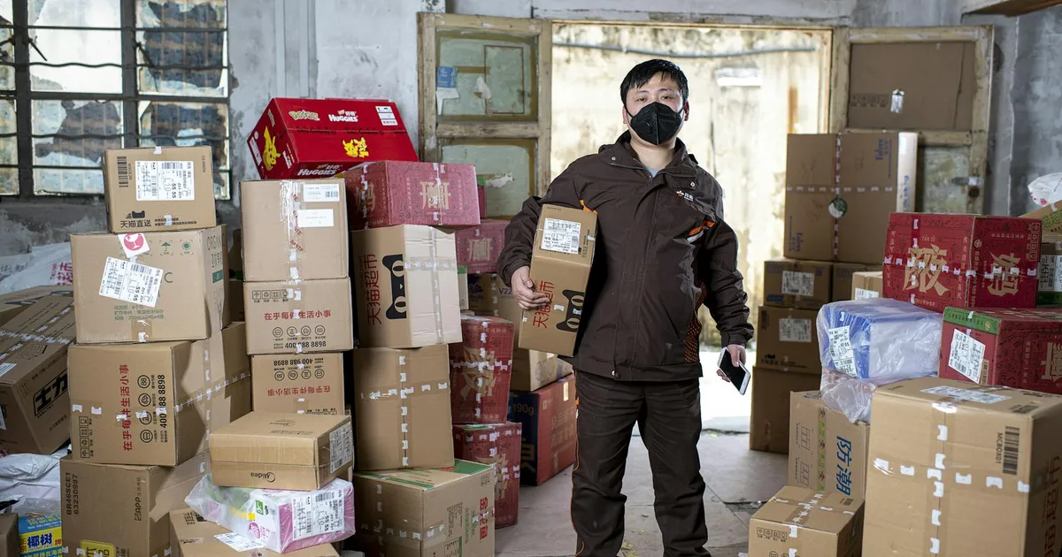 Delivery worker holding packages in a Wuhan warehouse, wearing a face mask.