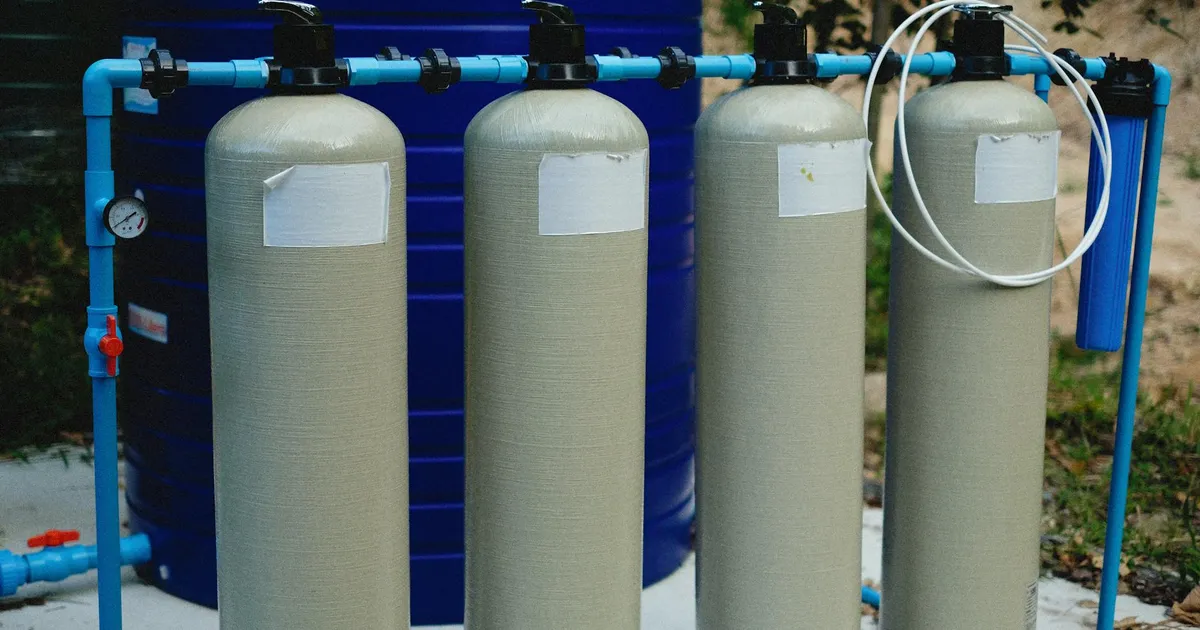 Four beige tanks in an outdoor water treatment setup with blue piping.
