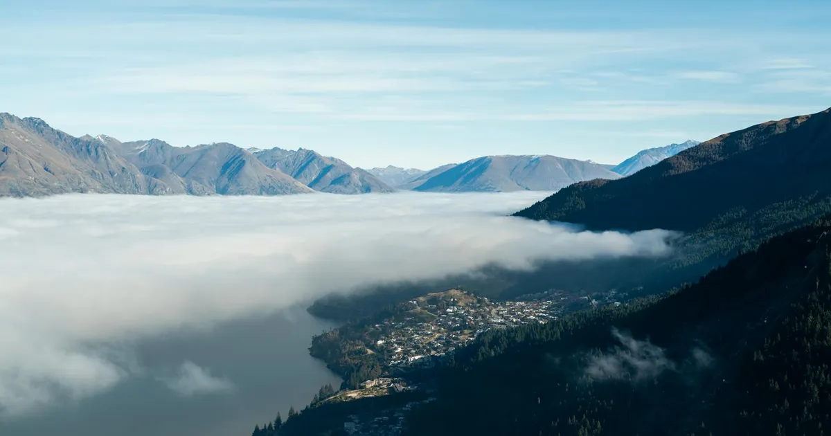 Stunning aerial landscape of Queenstown, New Zealand with mountains and misty clouds.