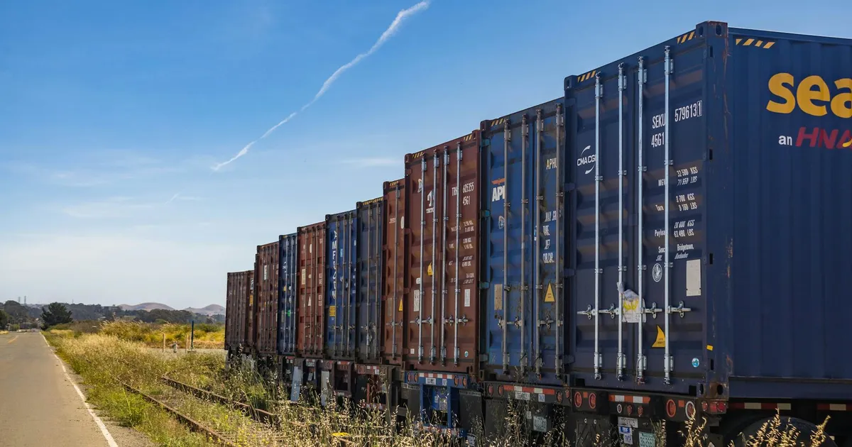 Colorful cargo containers on a freight train along a rural railway track under a clear blue sky.