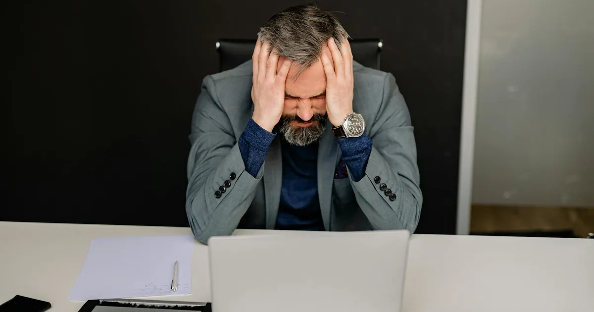 Businessman showing frustration with hands on head while working on a laptop in an office setting.