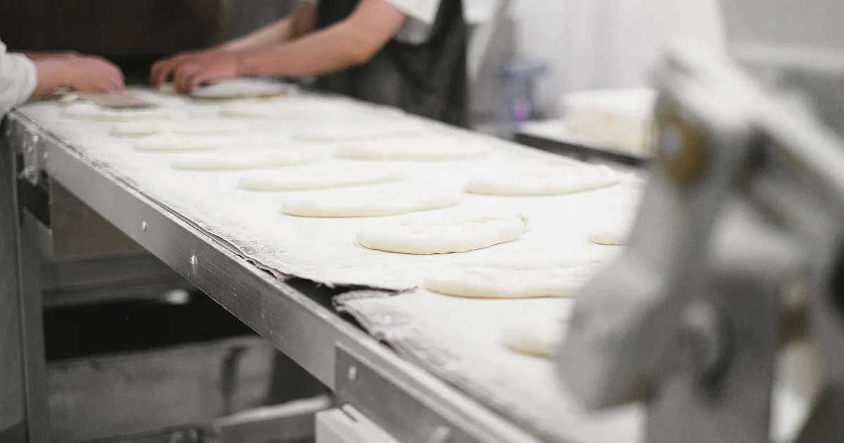 Bakery workers shaping dough pieces on a production line in an industrial setting.