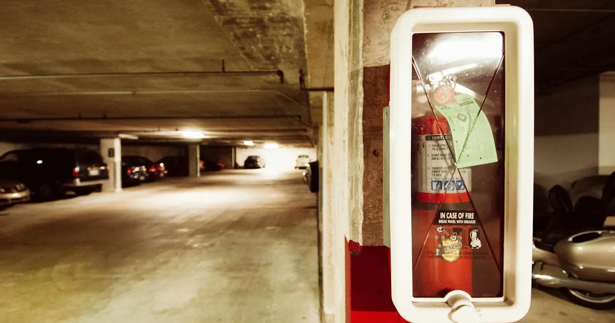 Fire extinguisher in an underground parking garage with parked cars.