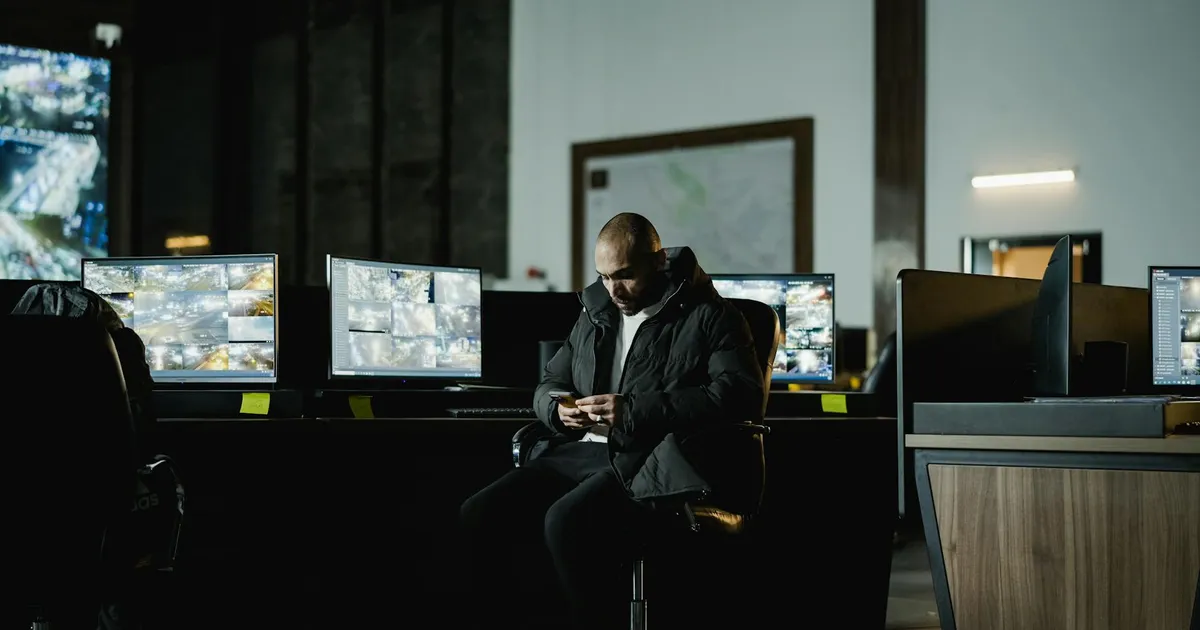 Security officer seated in a dimly lit control room, analyzing multiple surveillance screens.