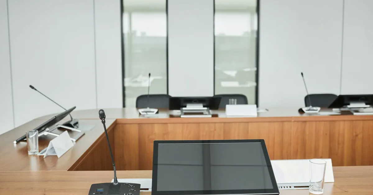 Empty conference room setup with microphones, monitors, and sleek wooden tables ready for meetings.