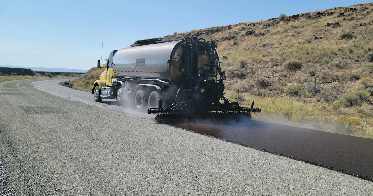 A road tanker applying asphalt on a rural road in Oregon under clear skies.