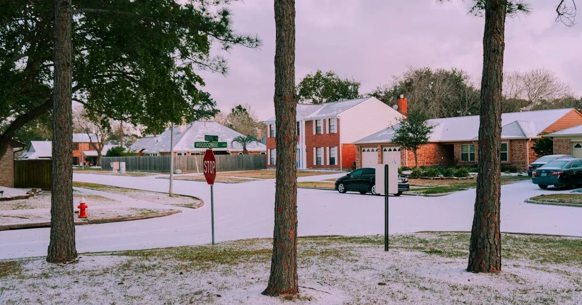 A serene suburban street covered in snow, featuring houses and trees on a winter day.