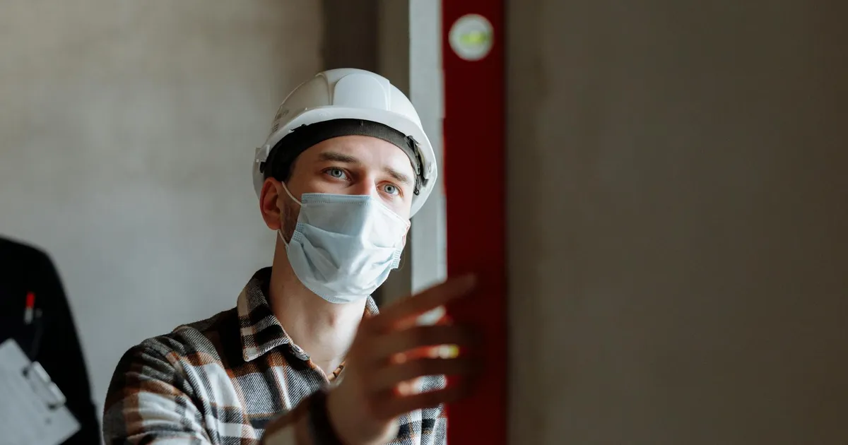 Man wearing a face mask and hard hat conducting safety inspection indoors.
