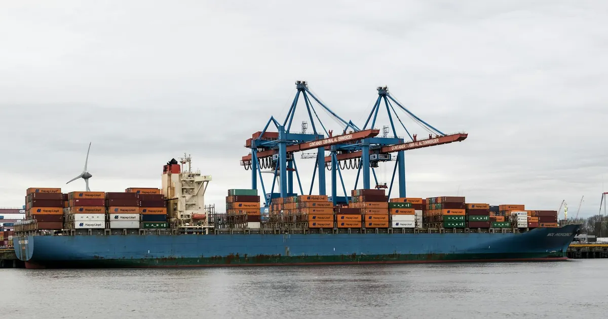 A container ship docked at Hamburg port surrounded by cranes and shipping containers.